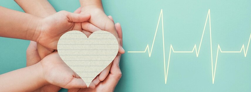 Mehrere Hände halten gemeinsam ein Herz aus Papier, rechts davon ist eine EKG-Kurve zu sehen.