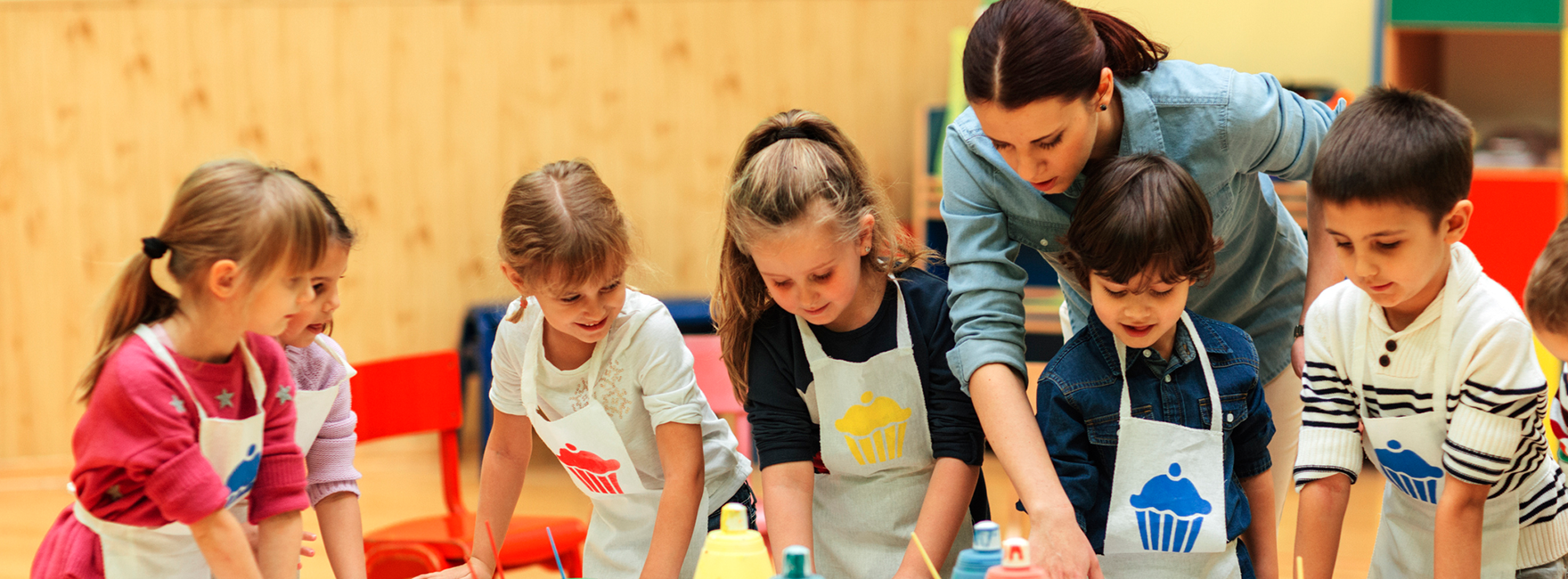 Eine junge Frau beugt sich über einen Tisch an dem mehrere Kinder mit Knete experimentieren. 