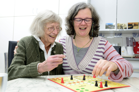 Eine ältere Dame und eine etwas jüngere Dame spielen gemeinsam das Gesellschaftsspiel Mensch ärgere dich nicht.