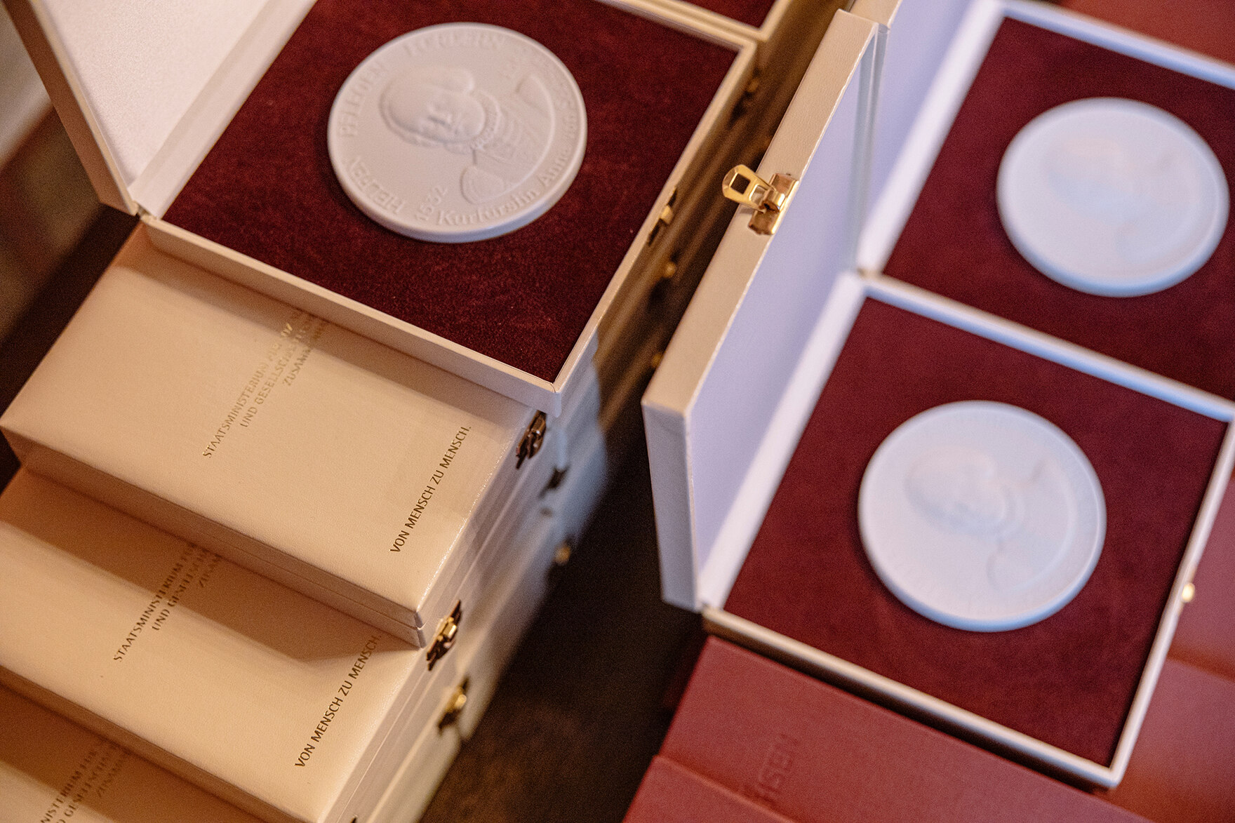 Zu sehen ist die Annen-Medaille mehrfach aufgereiht auf einem Tisch, in der Mitte steht eine einzelne Margerite.