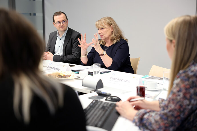 Ministerin Köpping sitzt mit weiteren Personen an einem Konferenztisch und gestikuliert.
